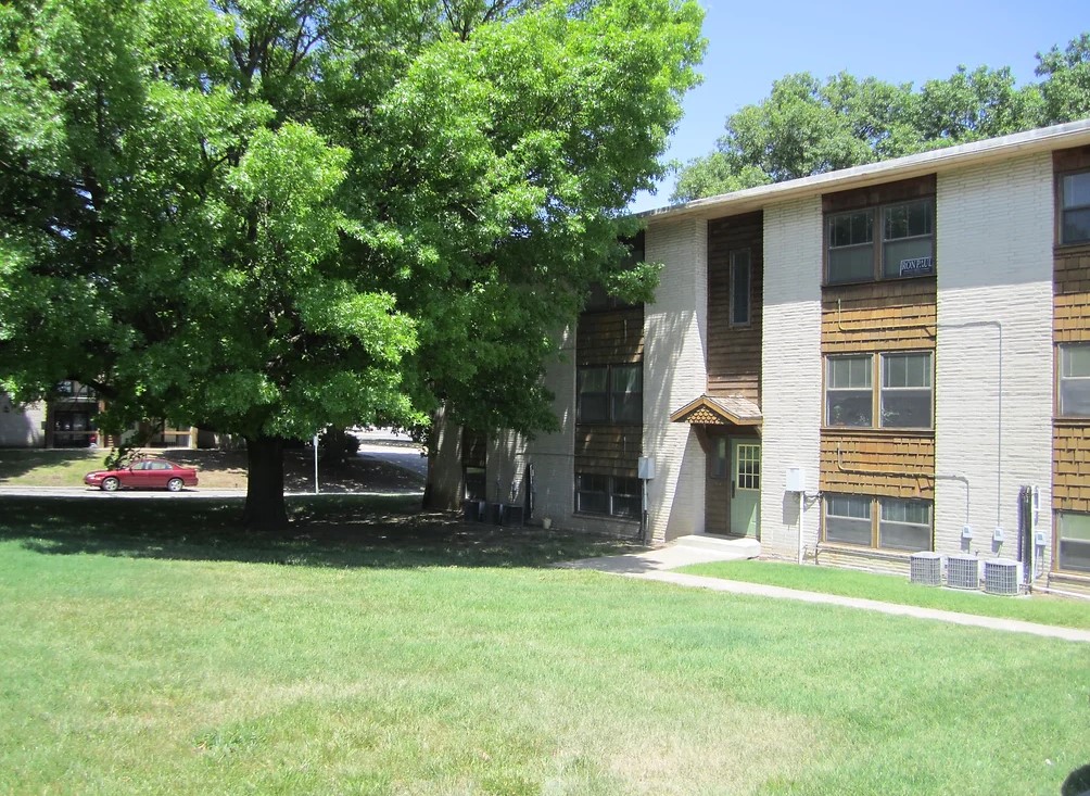 Angled front view of an apartment building with 4 balconies and an entrance in the middle. There is a bike sitting under the nearest balcony.